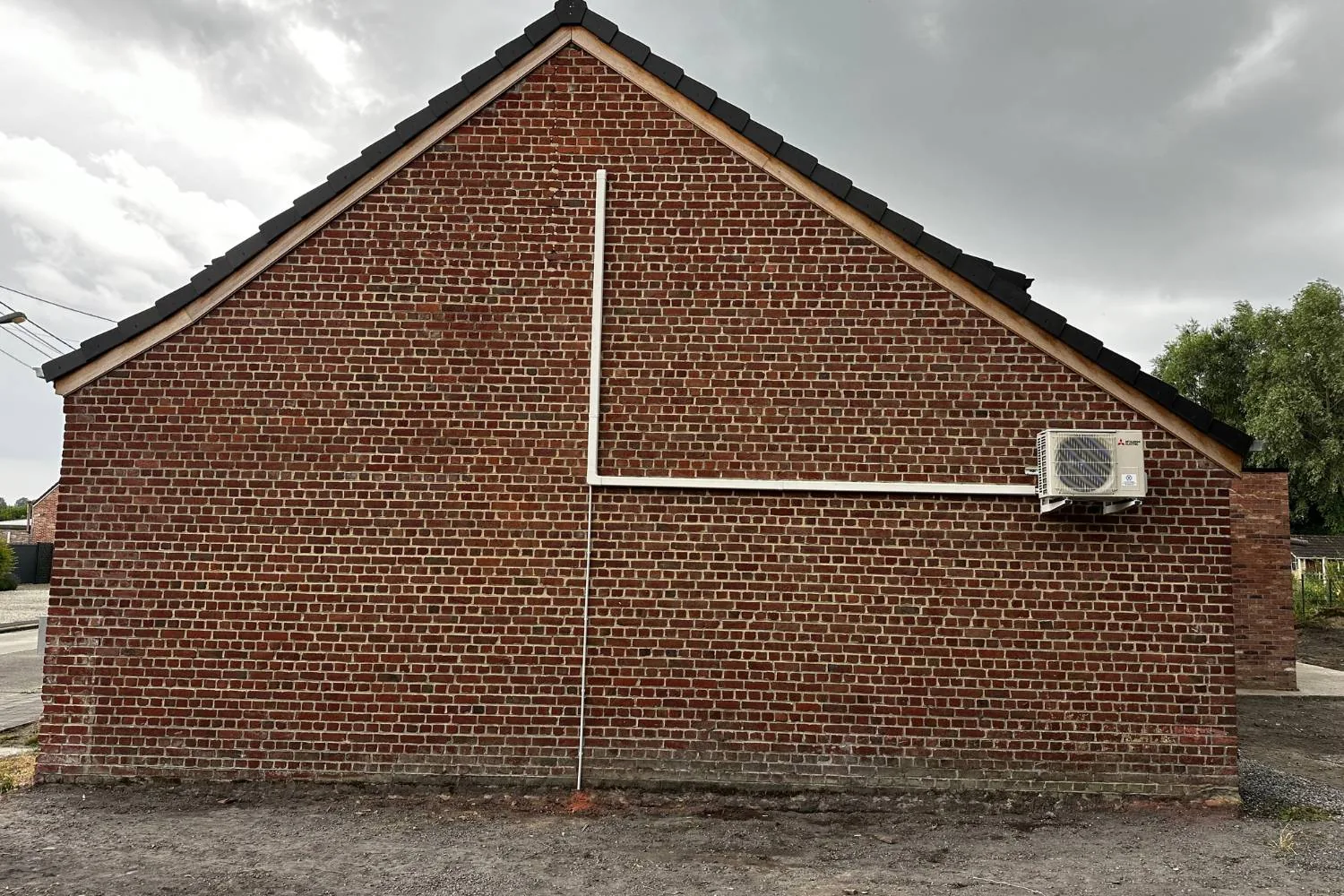Unité extérieure de pompe à chaleur air-air Mitsubishi Electric installée sur le pignon d'une habitation en Wallonie